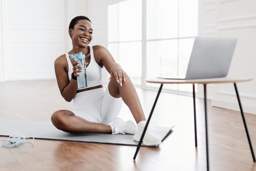 Woman drinking from a water bottle while on a Zoom call with her health coach