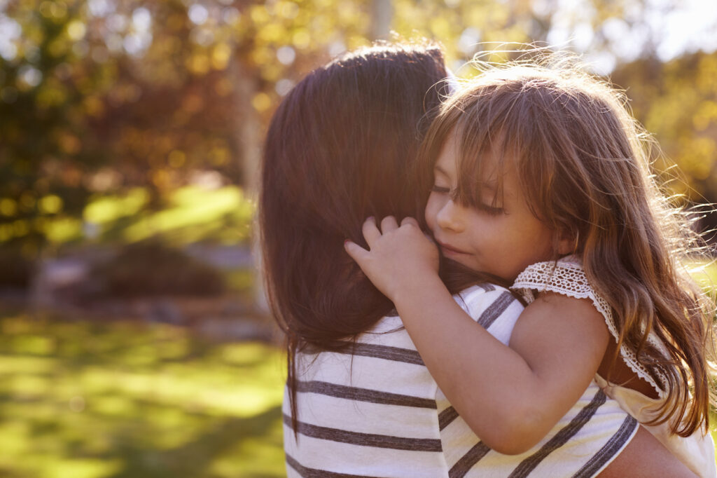 Mom comforting young daughter with loving hug in nature