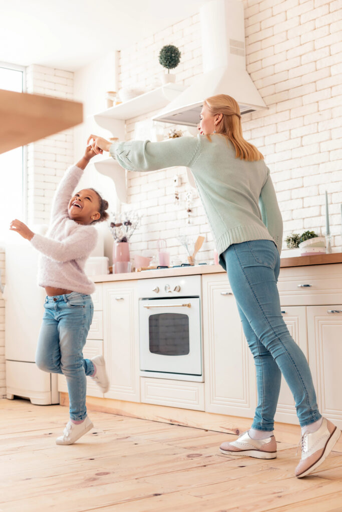 Young mother dancing with daughter in kitchen