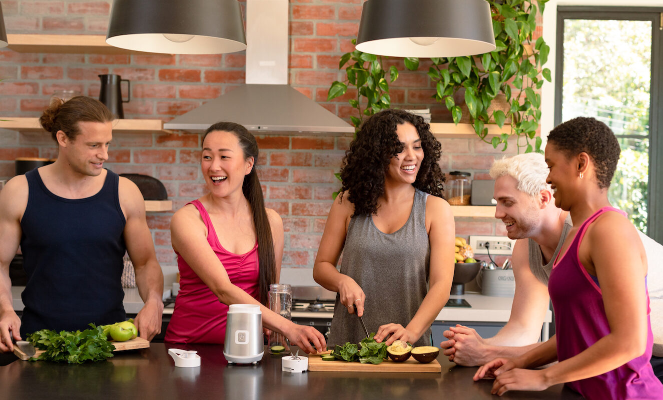 Group of friends gathered in kitchen cooking healthy meal while laughing