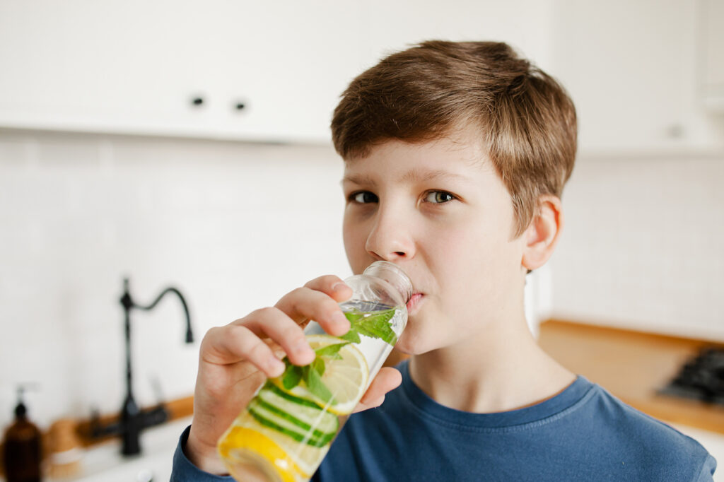 Teenage boy drinking from water bottle with lemon, lime and mint