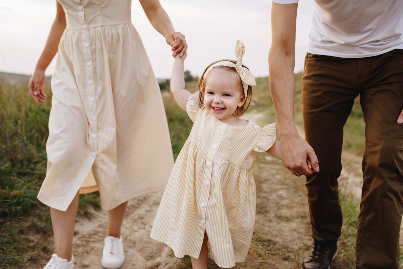 T1D family holding hands with young daughter walking in field