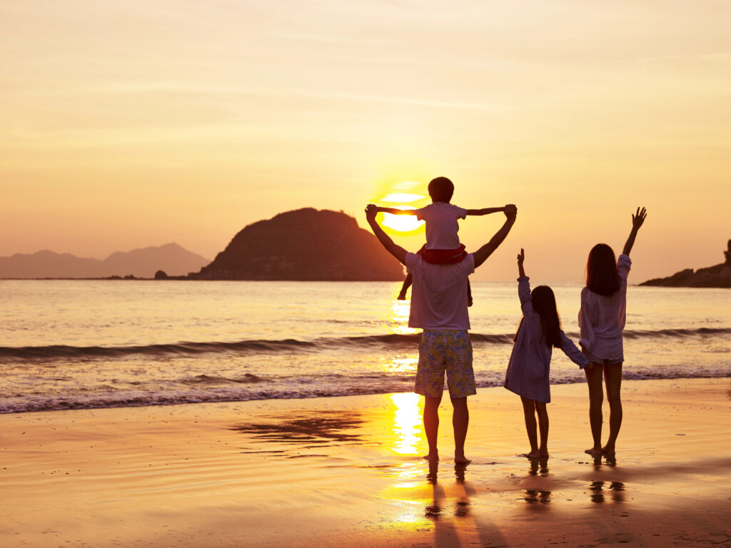 T1D mom support system standing on a beach with her family watching a sunset while holding hands