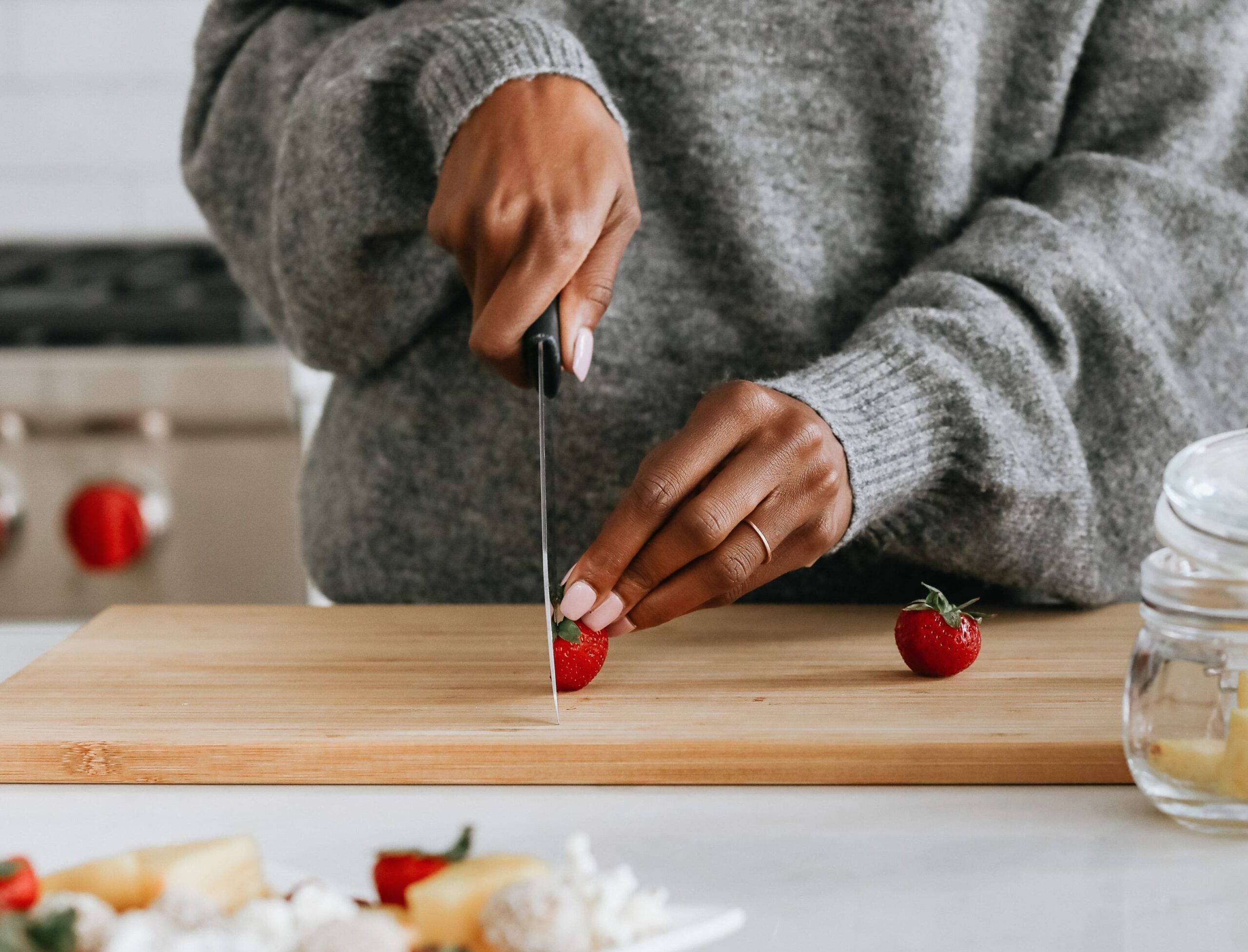 A woman slicing a strawberry in a bright kitchen, illustrating a simple food choice to support blood sugar balance and understand where does glucose go – Type Won Coaching™
